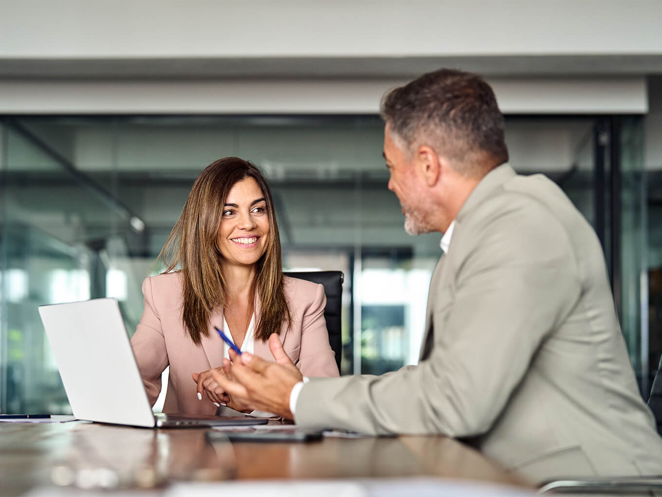 Ein älterer Versicherungsmakler im Gespräch mit einer jüngeren Frau in einem Büro.