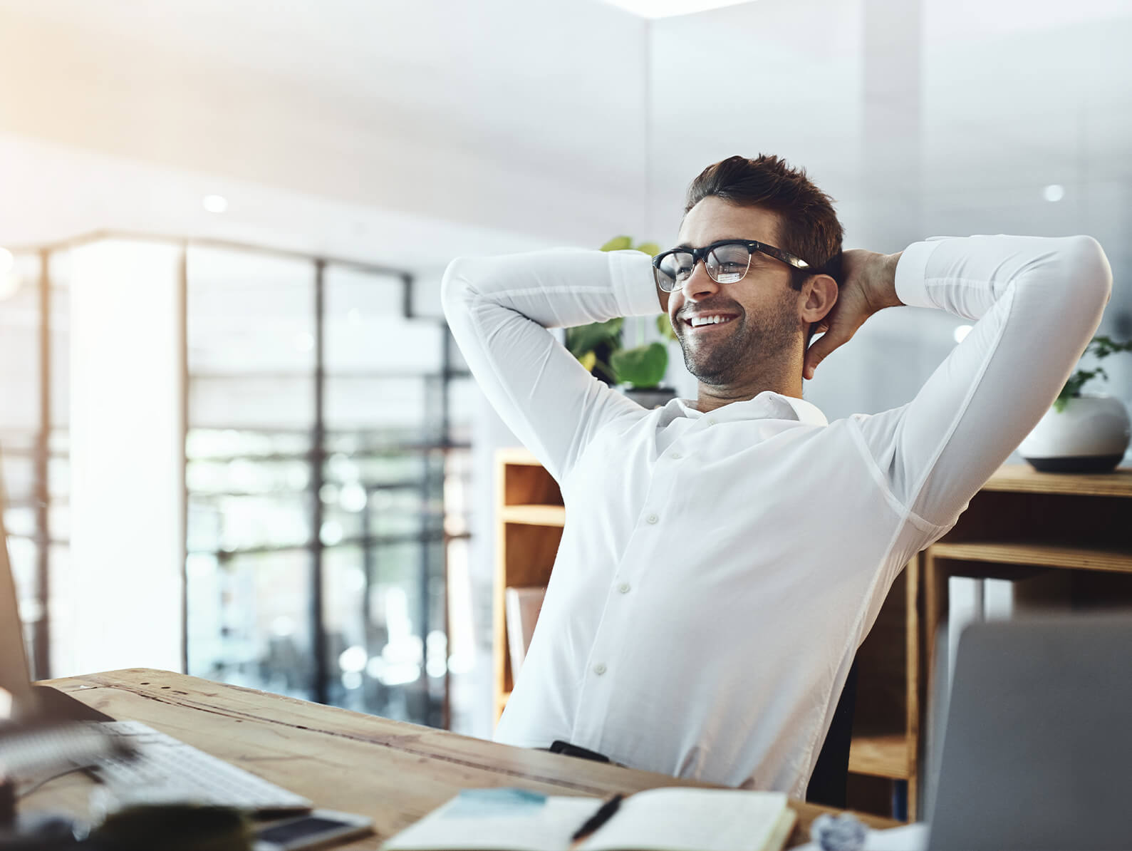 Versicherungsmakler sitzt dank der KI ViKI entspannt mit verschränkten Händen hinterm Nacken am Schreibtisch.