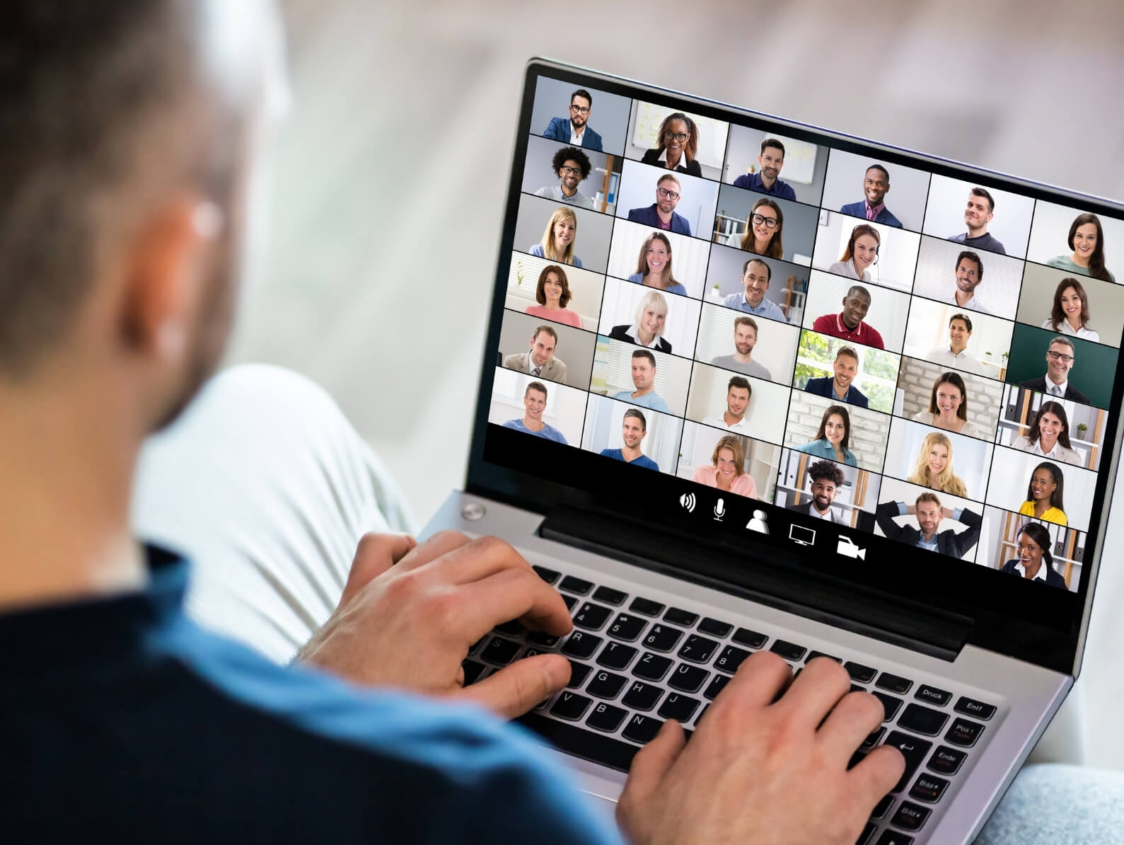 Ein Mann sitzt vor seinem Notebook, auf dessen Screen viele Teilnehmer eines Live-Webinars zu sehen sind